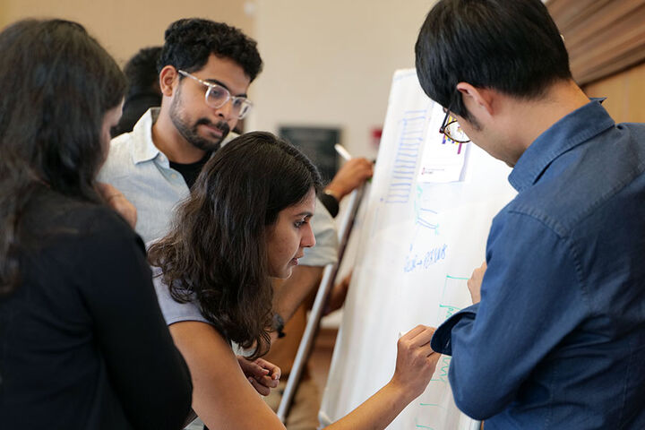 A group of students gathers around and makes notes on an easel pad.